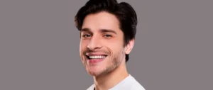 Smiling man with short dark hair, wearing a white shirt, against a gray background. He looks relaxed and happy.