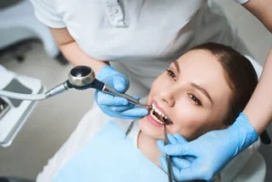 A smiling woman receives a dental check-up from a dentist wearing blue gloves. She is relaxed in a dental chair, conveying a calm and professional tone.