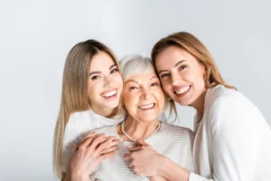 Three women, representing different generations, smile warmly. The older woman is in the center, showing a family bond and joyful connection.