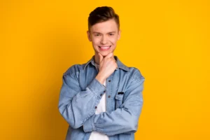 A smiling person in a denim jacket poses confidently against a vibrant yellow background, conveying a cheerful and upbeat mood.