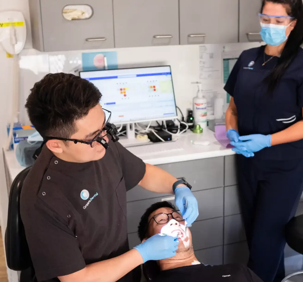 Dentist examines a patient's mouth while a nurse looks on, both wearing protective gear.