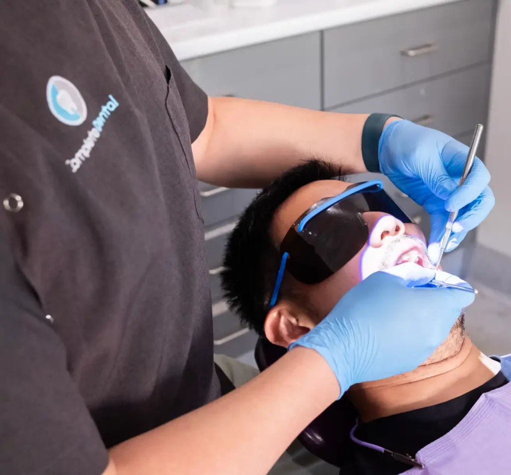 A dentist wearing gloves and a uniform examines a patient's mouth using dental tools.