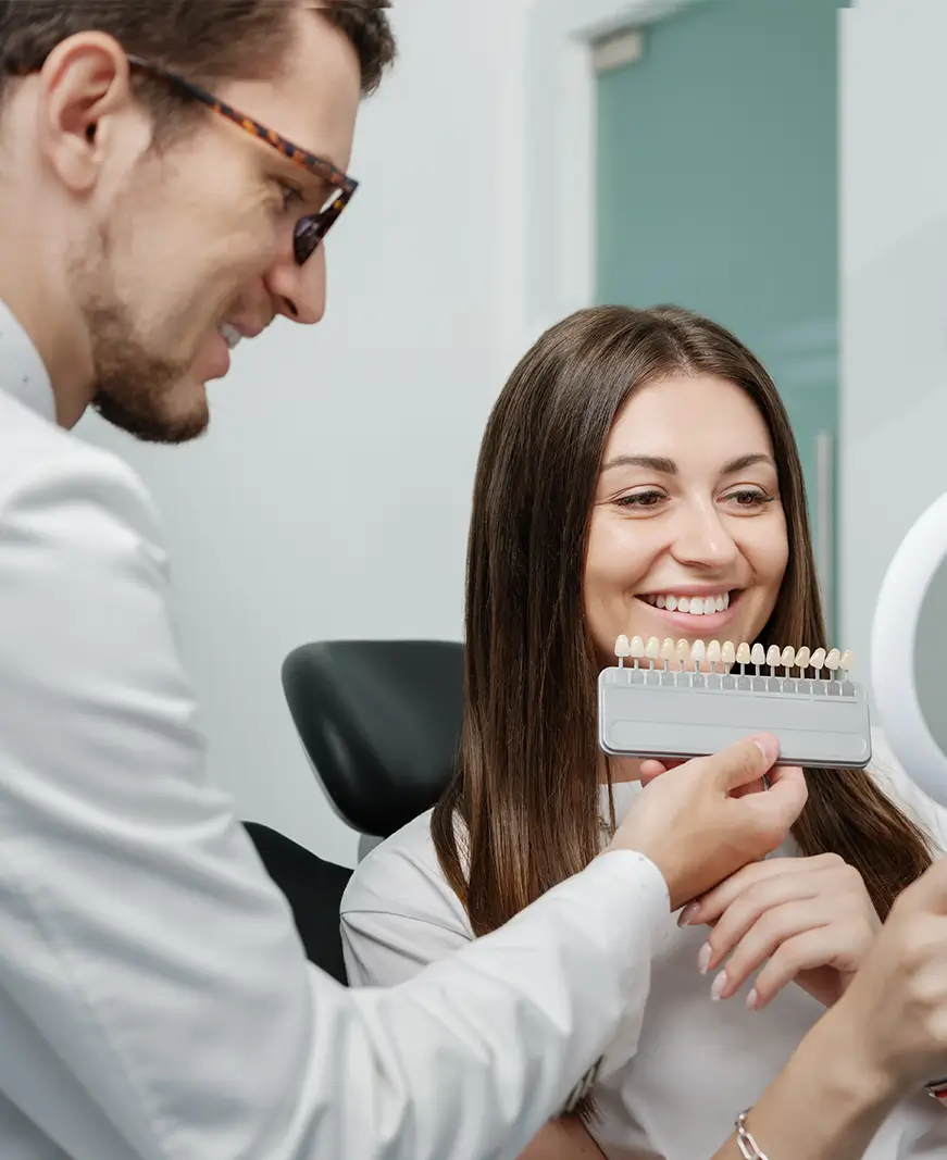 A dentist showing a smiling woman a set of tooth shade samples.