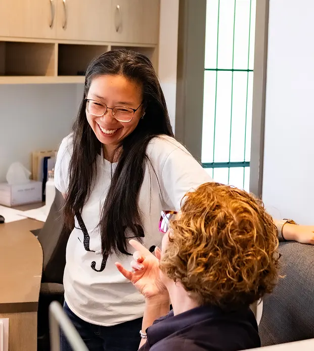 Dr Alice smiling warmly at a seated person, creating a welcoming atmosphere at a reception desk.
