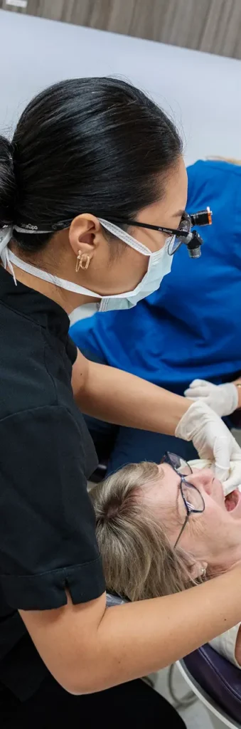 A dentist with glasses and a mask, examine her patient's teeth.
