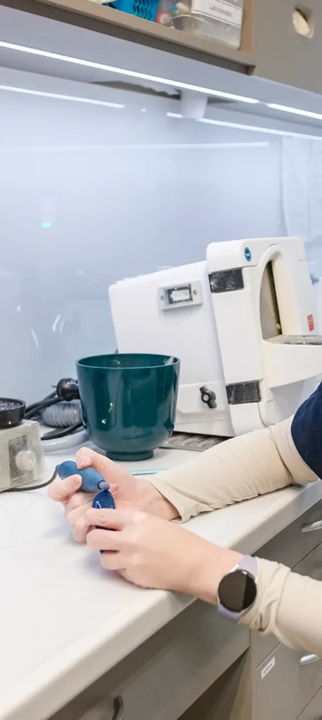 A person holding dental equipment in a clinic setting, next to a teal cup and dental machinery, conveys a professional, clinical environment.